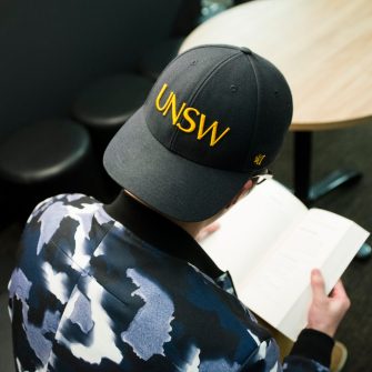 Photograph of someone wearing a UNSW hat reading a book