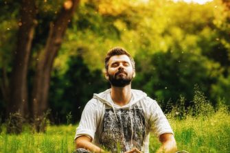 A bearded person meditating on green grass in the park