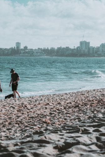 Two people stroll along a beach with city skyline in the background