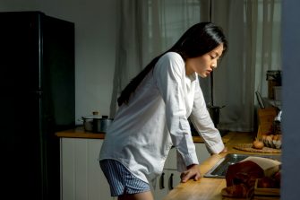 Depressed young person standing in the kitchen with stressed face
