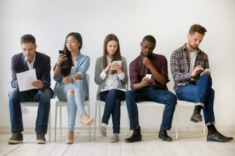Diverse millennial  people waiting in queue sitting on chairs using devices