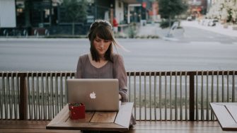 Young woman sitting at outdoor cafe table with laptop