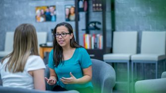 A woman in her early 30s explains something to a client who is sitting across from her. She looks passionate about what she is saying.