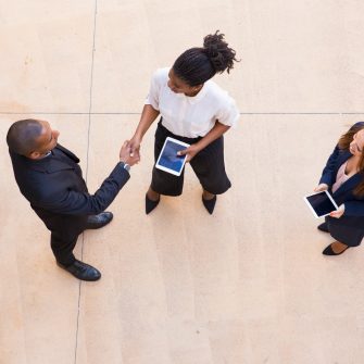 Business partners meeting in office hall. Top view of black man and woman in formal clothes shaking hands, holding tablet and talking. Partnership concept