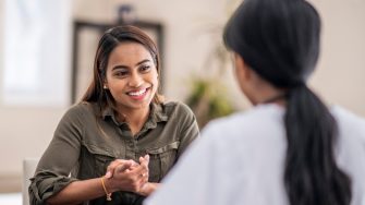 A stressed-out woman is chatting with her mental health counselor. She is explaining her problems. She is staying positive with a smile.