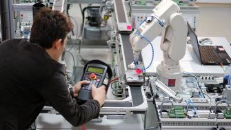 Man is working to control a robotic arm which is integrated on smart factory production line. industry 4.0 automation line which is equipped with sensors and robotic arm. Selective Focus.