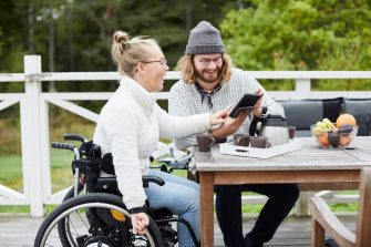 Woman in a wheelchair looks at tablet device her friend has