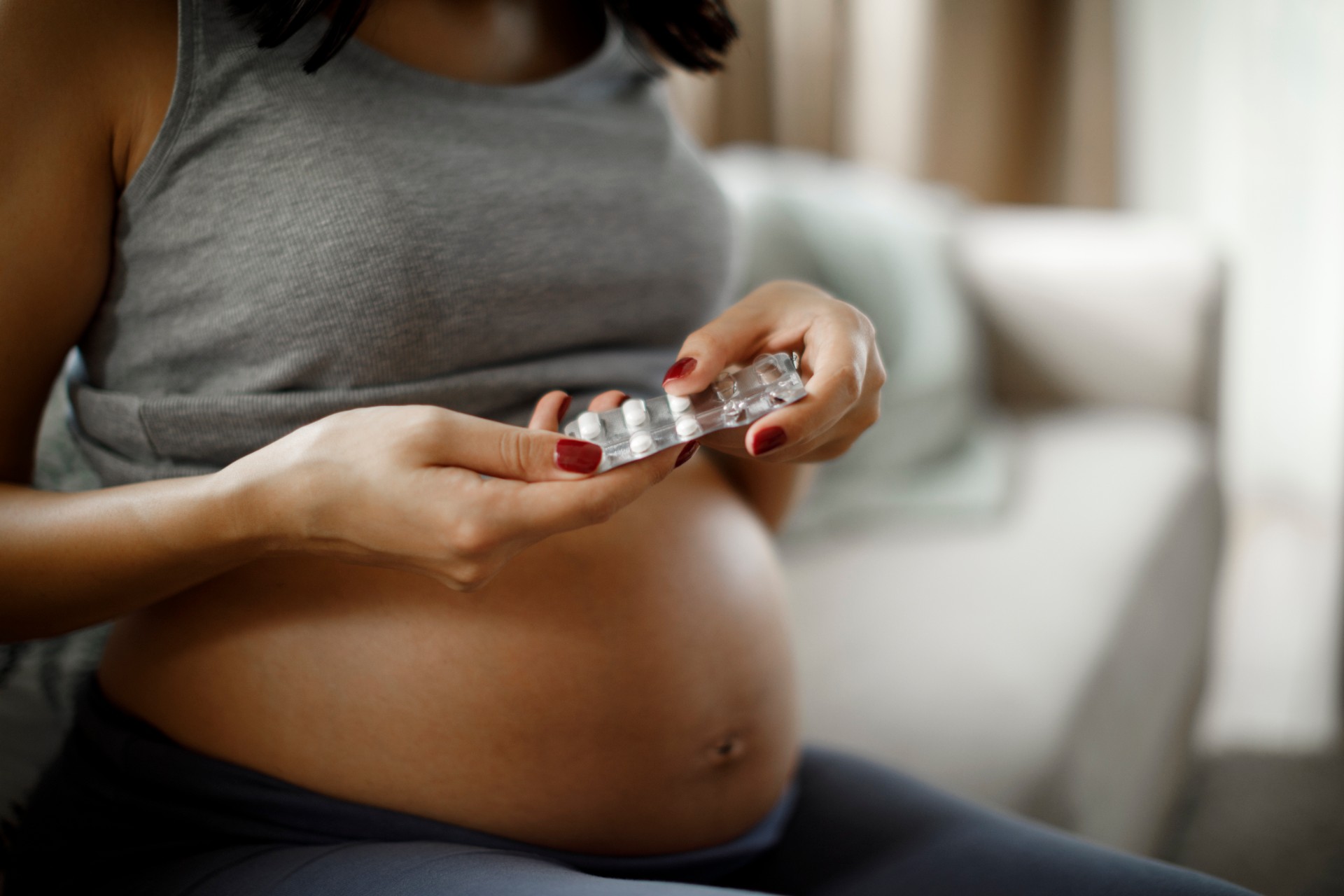 A pregnant woman taking a pill while sitting on her lounge at home