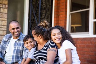 An Indigenous Australian family sitting together on their front porch smiling together