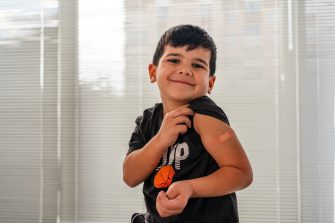 Vaccinated young boy smiling while showing bandaid on arm after a needle