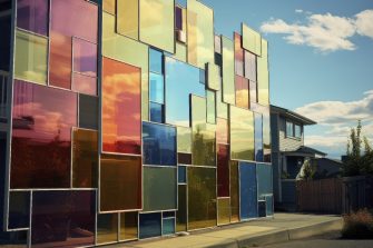 The wall of a building with multiple different sized oblong panels of different colours, shining in the sun.