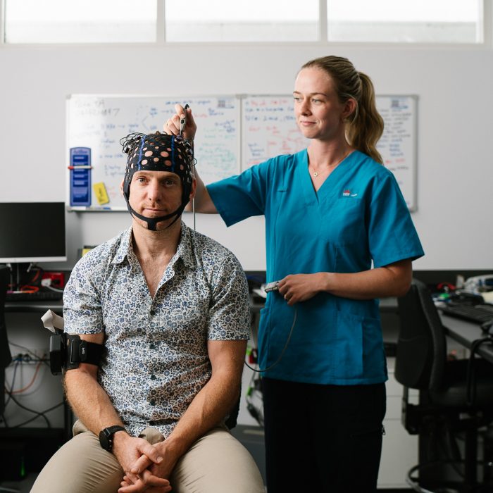 Patient wearing a mesh cap with different nodes sitting in an office as a researcher uses a motion mapping tool that looks like a pen