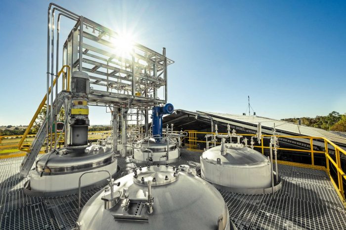 Large biofermentation tanks on a rooftop with walkways around them. Blue sky