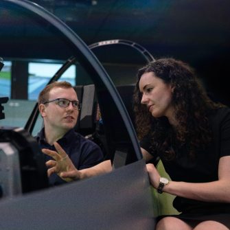 Man in flight simulator cockpit talking to woman sitting next to him