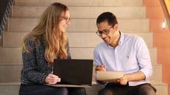 Two people sitting on stairs looking at laptop