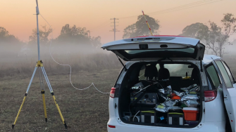 Car parked in misty field wiht boot open and large antenna set up nearby