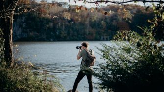Man with backpack taking picture beside lake