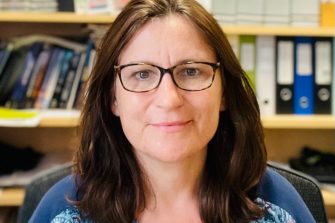 Professor Lisa Alexander sits smiling in front of a bookcase crowded with files.