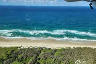 Coast line looking toward the ocean with green bushland in foreground,  sand and ocean in backgroun