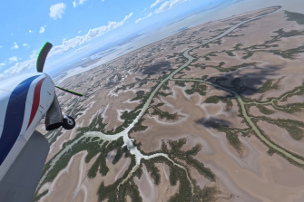 Light airplane in flight over mudflats