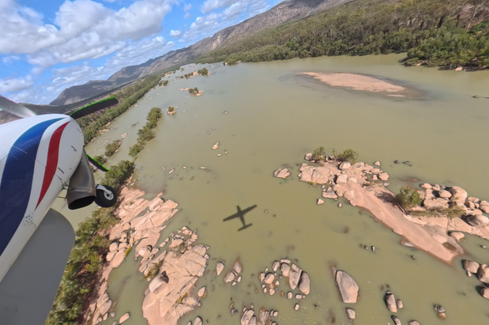 Light airplane in flight over water and rocks