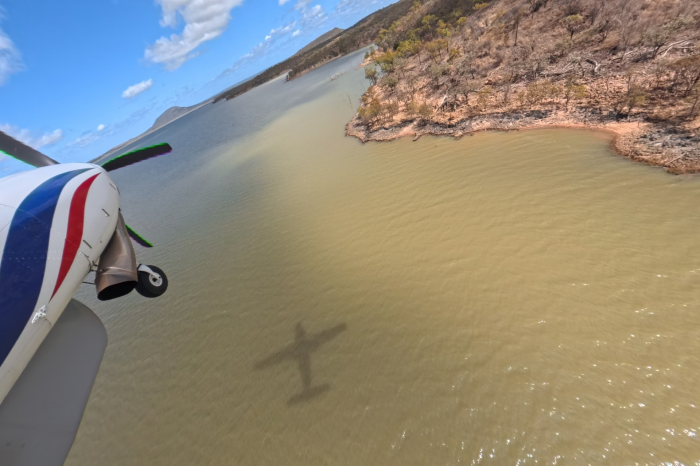 Light airplane in flight over water and land at right