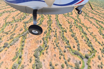 Light airplane in flight over water channels with red earth and trees