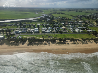 Aerial view of ocean in foreground looking houses, a water channel and sky in the distance