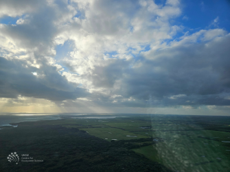 Aerial view of green landscape, water in distance and a cloudy sky