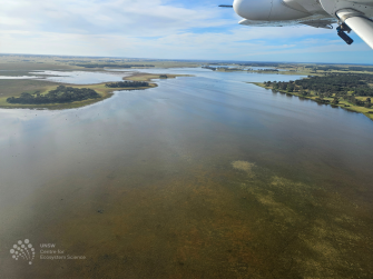 Aerial view of vast water with some land and cloudy sky in the distance