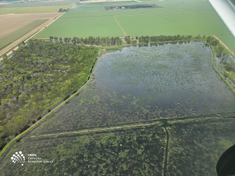 Aerial view of flooded wetland and green fields behind