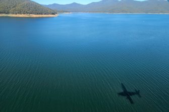 Aerial view of vast waterbody with shadow of light plane and mountains and sky in distance