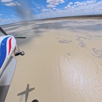 View of front section of light plane over vast water body with land and sky in distance