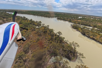 View of front section of light plane over bushland and water course at right with some green vegetation