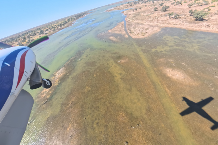 View of front section of light plane over water channel with red earth and some green vegetation either side