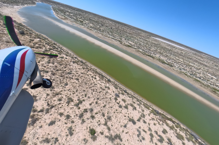 View of front section of light plane over water channel with red earth and some green vegetation either side