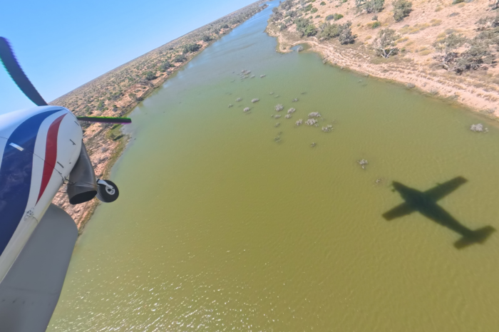 View of front section of light plane over water channel with red earth and some green vegetation either side