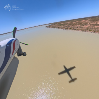 View of front section of light plane over brown water with shoreline and sky in the distance