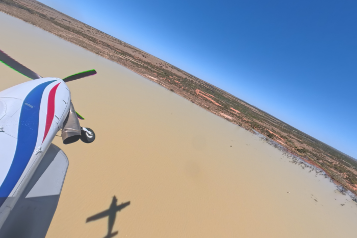 View of front section of light plane over brown water with shoreline and sky in the distance