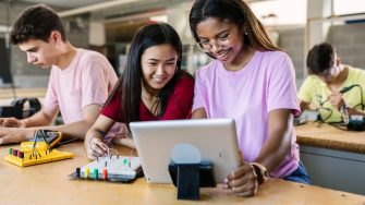 Group of diverse teenage students learning together to build electronic circuits at high school - Asian and african american female classmate working at technology class
