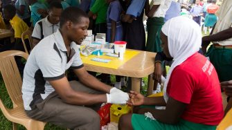 Nkokonjeru, Uganda. June 22 2017. A young man testing a girl for HIV by pricking her finger and drawing blood.