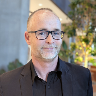 Portrait image of Dr Wesley Morgan wearing a black suit and dark brown framed optical glasses