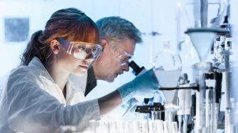 Health care researchers working in life science laboratory. Young female research scientist and senior male supervisor preparing and analyzing microscope slides in research lab.