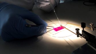 Gloved hand performing experiment on small square of pink material