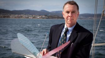 Trevor McDougall stands on a boat holding a wooden butterfly