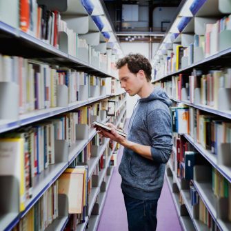 young student reading book between the shelves in the library