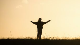 Silhouette of a person standing in a field spreading out their arms