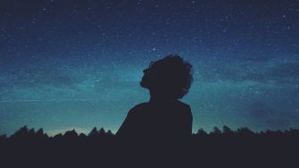 Silhouette of man looking throughfully at starry sky