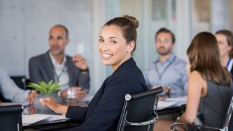 Young beautiful businesswoman with colleagues sitting in a modern board room. Proud smiling business woman sitting during a meeting and looking at camera. Portrait of a happy businesswoman with executives working.