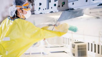 Student in lab with yellow lab coat, gloves, protective goggles and hairnet